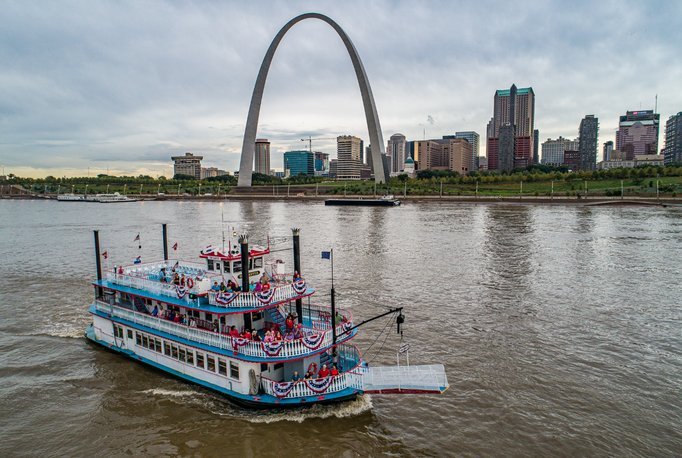 View from above of the Tom Sawyer Riverboat cruises on the Mississippi River in front of the Gateway Arch and St. Louis skyline.