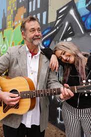 An older man holding a guitar and a younger female