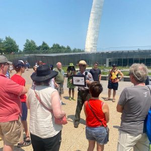 Park ranger holding a photo and standing with a group of people in front of the Arch