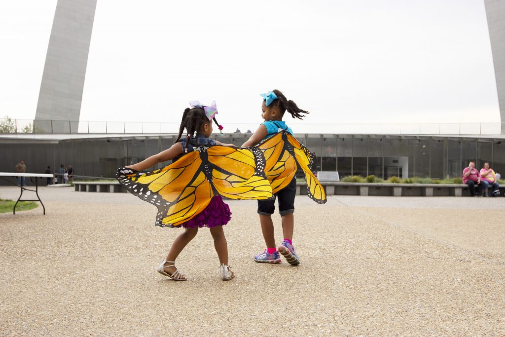 Two young African American girls with butterfly wings playing in front of the Arch