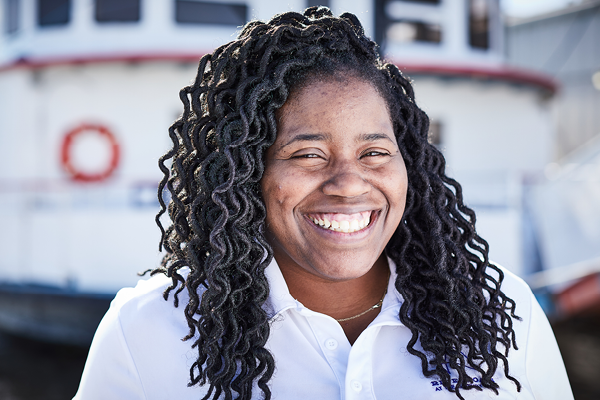A female Riverboat staff member smiles for a portrait standing in front of the Tom Sawyer.
