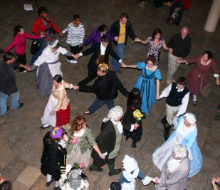 A few dozen people dance while holding hands, some dressed in Victorian formal wear, during the Twelfth Afternoon Ball event at the Gateway Arch.